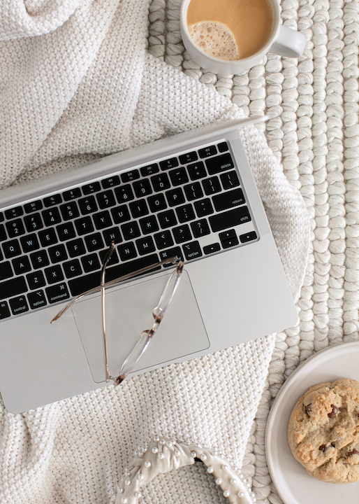 Illustrasjon på artikkel om å lage nettside i Wordpress, eller velge noe annet. En laptop er omringet av en cookie og en kaffekopp. Mykt, hvitt teppe på gulvet og et pledd laptopen står på.